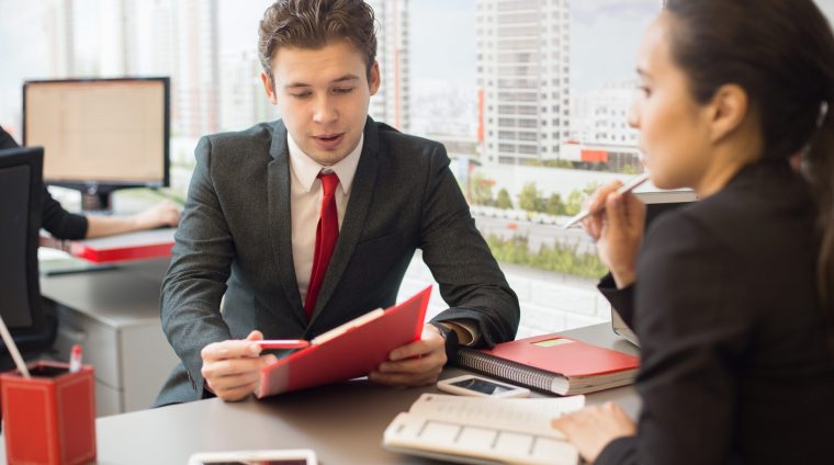 Managers in Real Estate Agency Portrait of young businessman talking to colleague discussing work during meeting in real estate agency