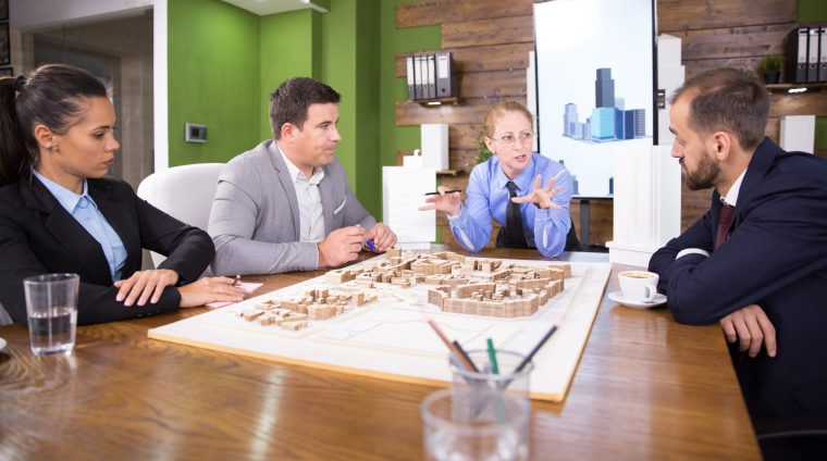 Middle age real estate developer in a meeting with construction engineers Middle age real estate developer in a meeting with construction engineers. Mini town. Building model.