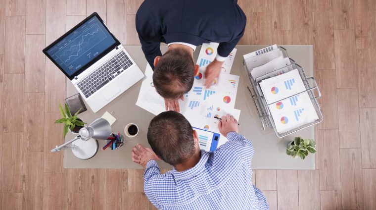 Top view of businessman analyzing management graphs discussing company strategy Top view of businessman analyzing management graphs discussing company strategy during businessmeeting in startup corporate office. Partners working at investments presentation during partnership